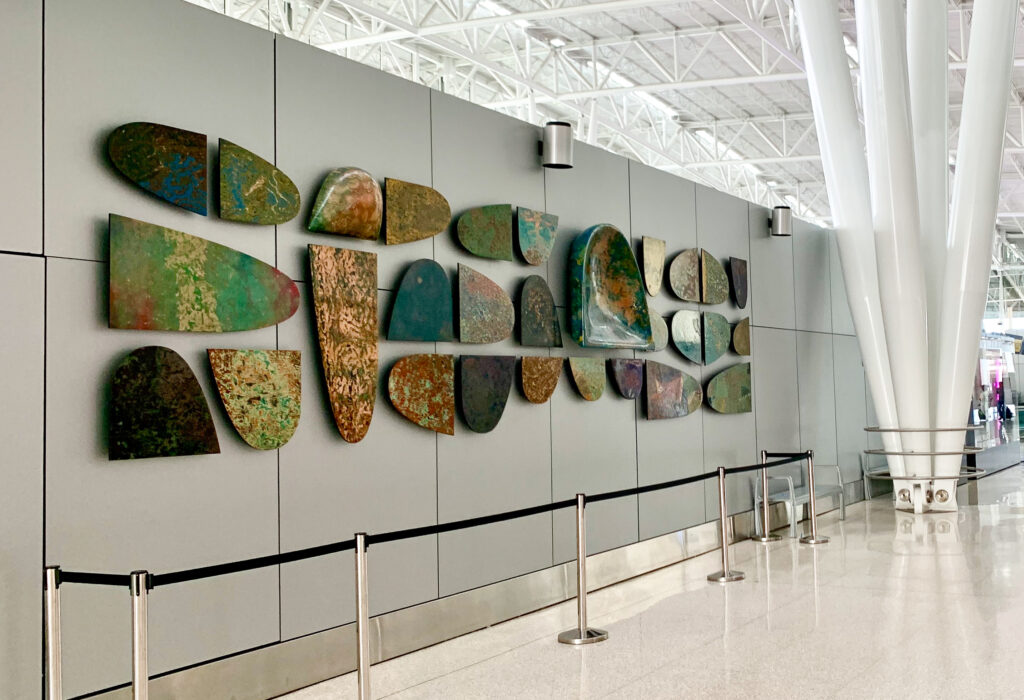 A wall with an assortment of three-dimensional works of varying sizes. They have abstract patterns made of a range of colors from yellows, greens, blues, and browns.