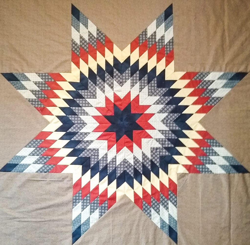 A quilt with an eight-point star pattern made of browns, greys, red and yellow.