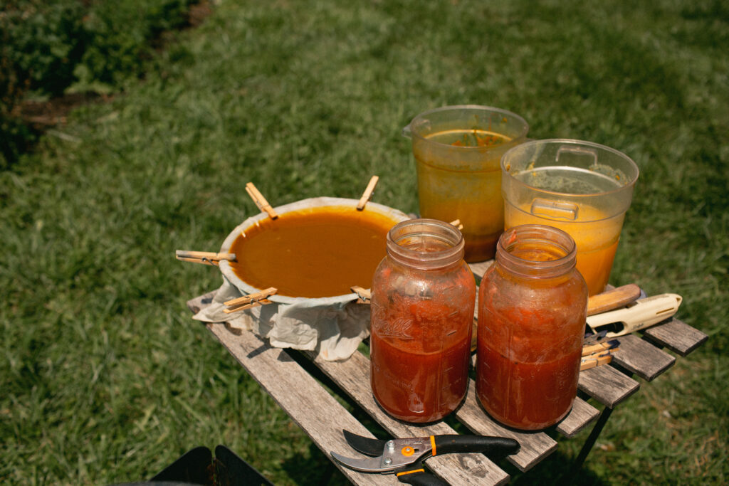 A table with an assortment of jars and small buckets containing natural dye and pigments of reds and yellows.