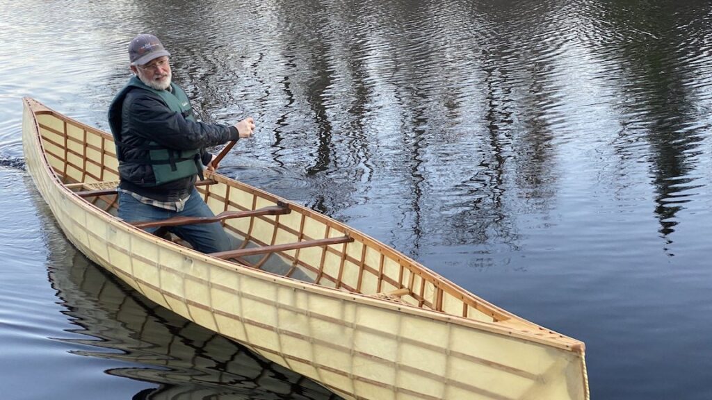 A person rowing a freshly made boat prototype in a river.