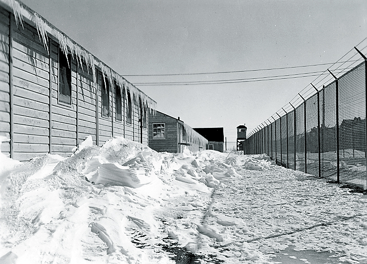 A black and white photo of a prison camp covered in ice and snow with barbed wire and fence visible