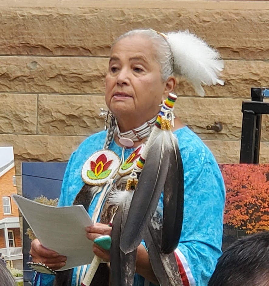 A Chippewa woman wearing regalia speaks with papers in her hands
