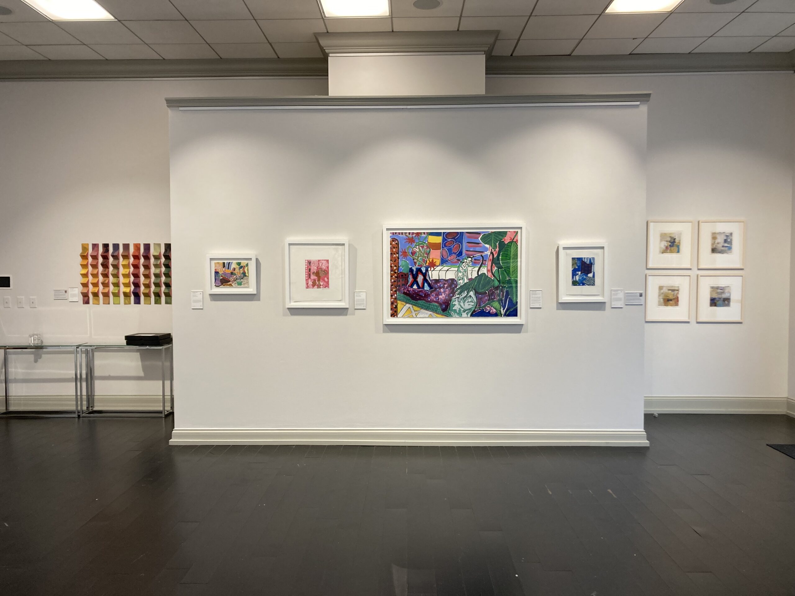 A gallery space featuring several colorful framed works of art hung on the walls.