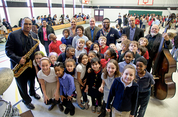 A person with a saxophone stands with a group of young people in a a gymnasium.