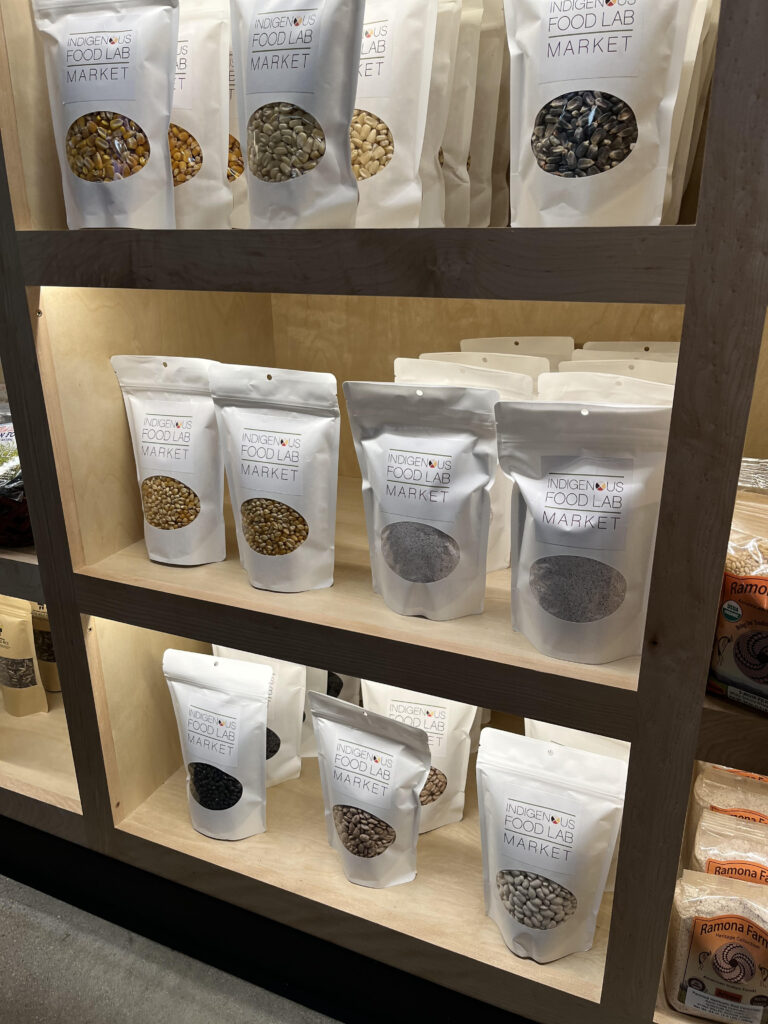 Packages of seeds, labeled Indigenous Food Lab Market are displayed on shelves.