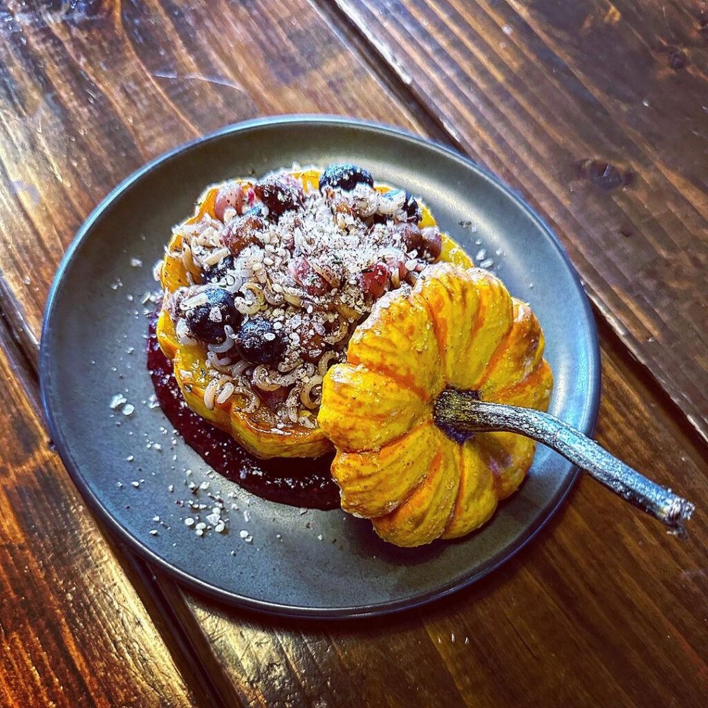 A mini pumpkin, sliced in half, with jam and other garnishes, displayed on a plate.