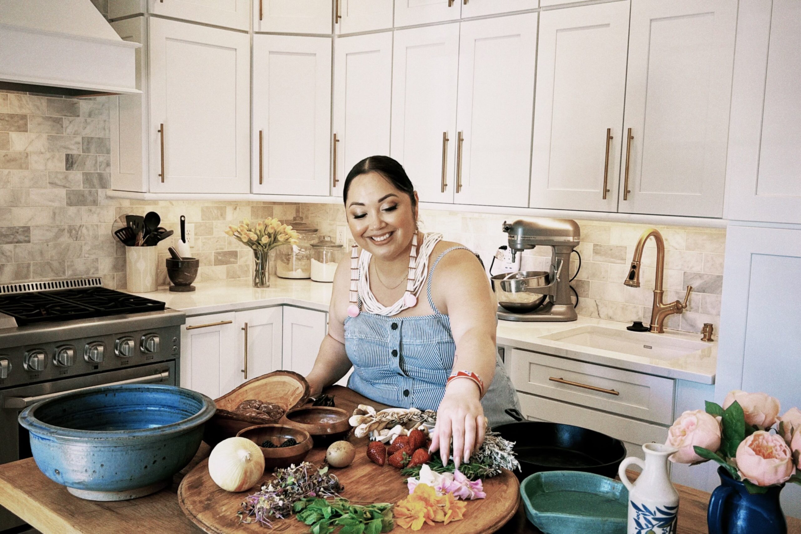 A smiling home chef displays an assortment of fresh ingredients on a wood cutting board.