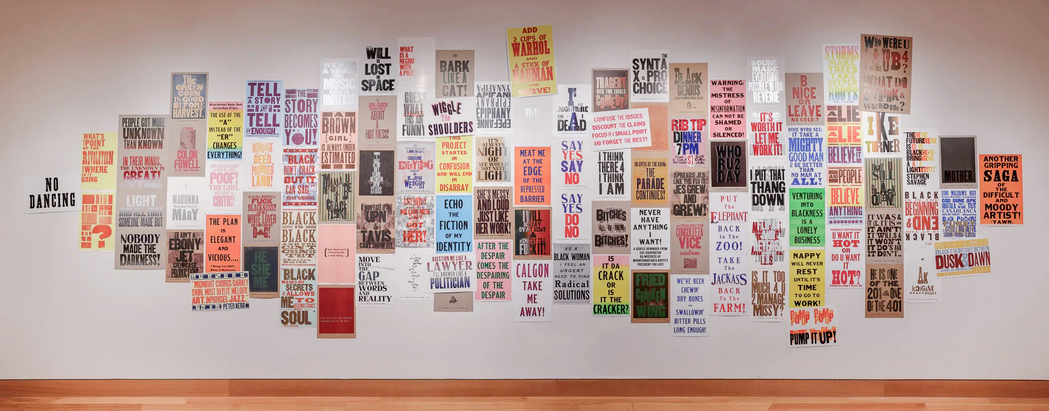 A large white is covered, from almost floor to ceiling, in multi-colored text-based letterpress posters as part of an art installation.