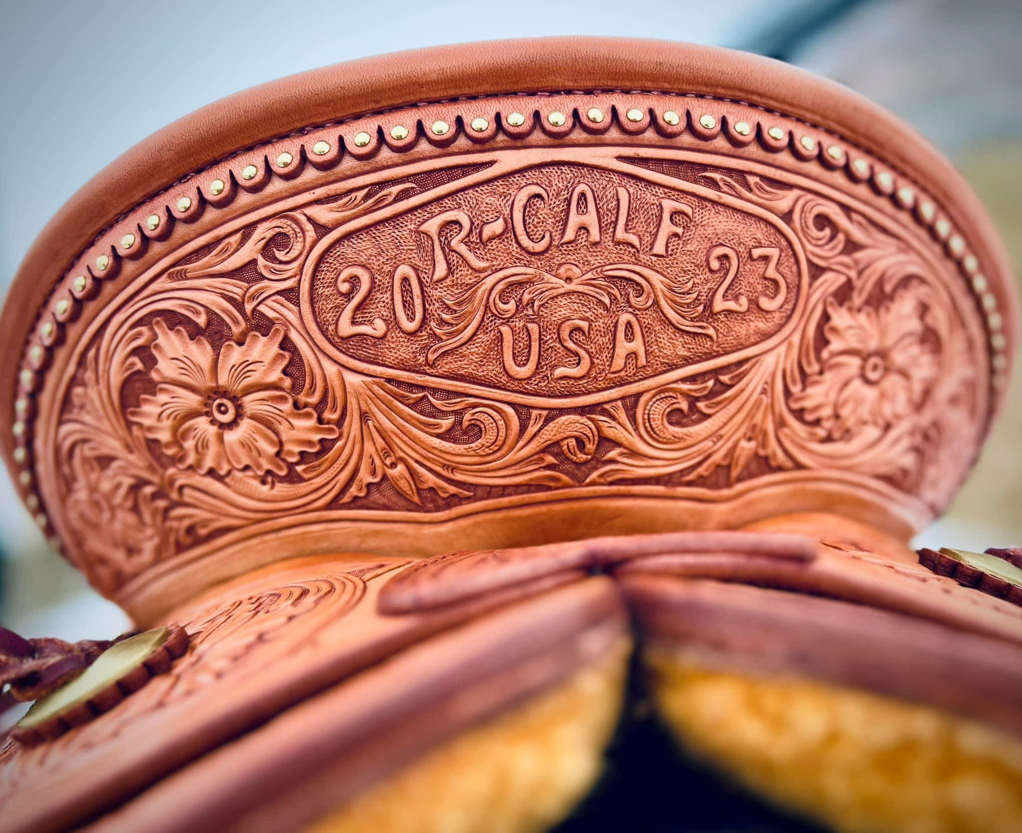 A seat section of a leather saddle with ornate flowers and designs, and stylistic lettering that reads "R-CALF USA 2023"