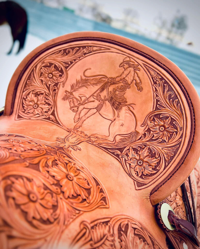 An ornately designed leather saddle with hand-carved patterns of flowers and a drawing of a rider on a horse.