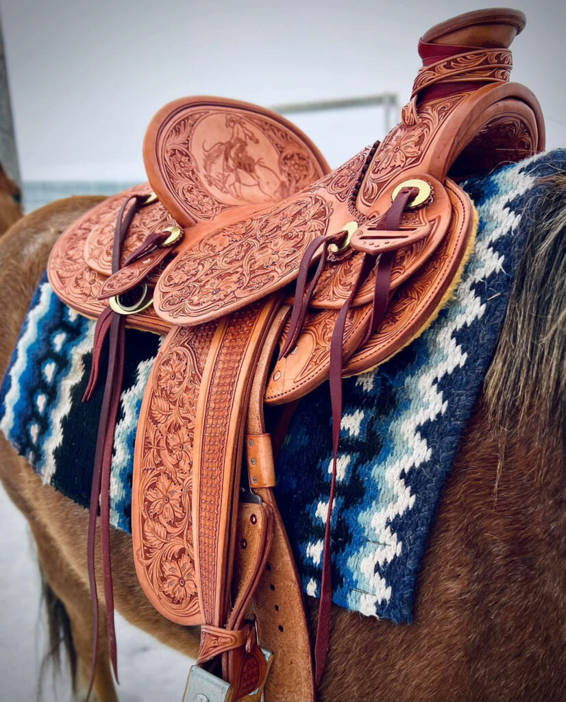 A leather saddles rests on the back of a brown horse over a blue woolen blanket.