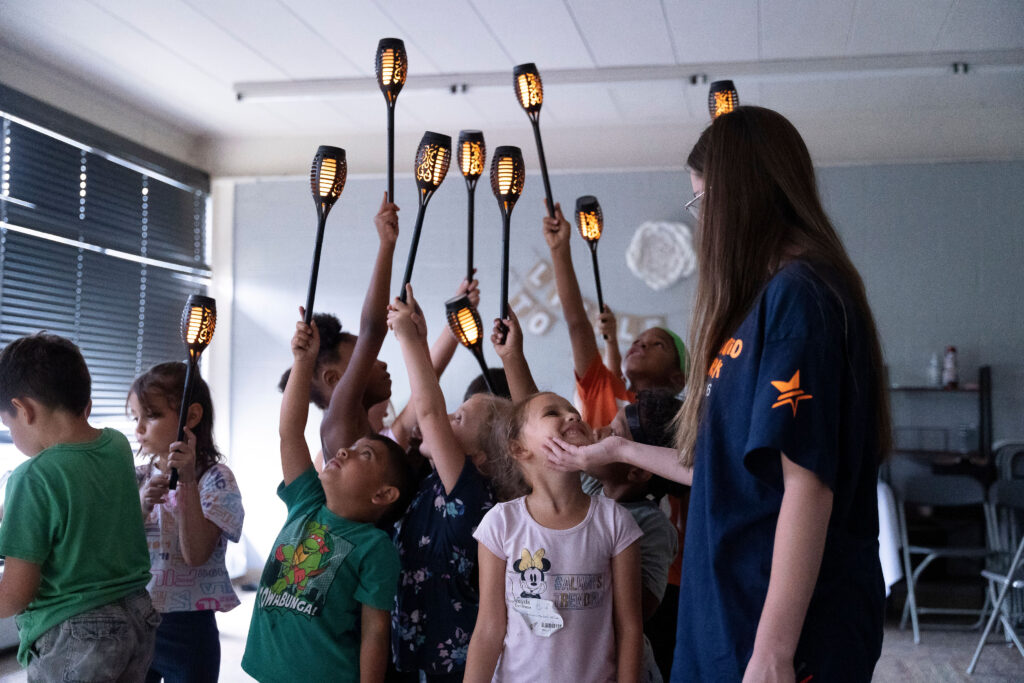 A group of young students hold lanterns up towards the ceiling.