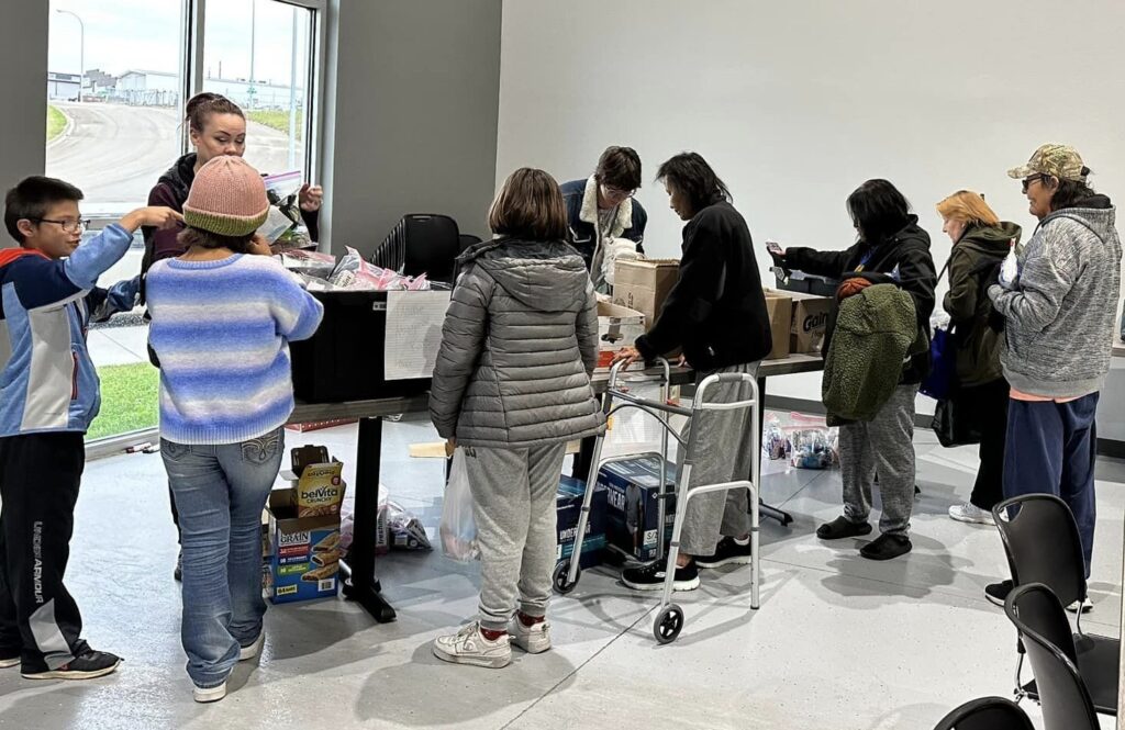 Several people grabbing bags of various food items, first aid supplies, and hygeine products from a long table filled with boxes.