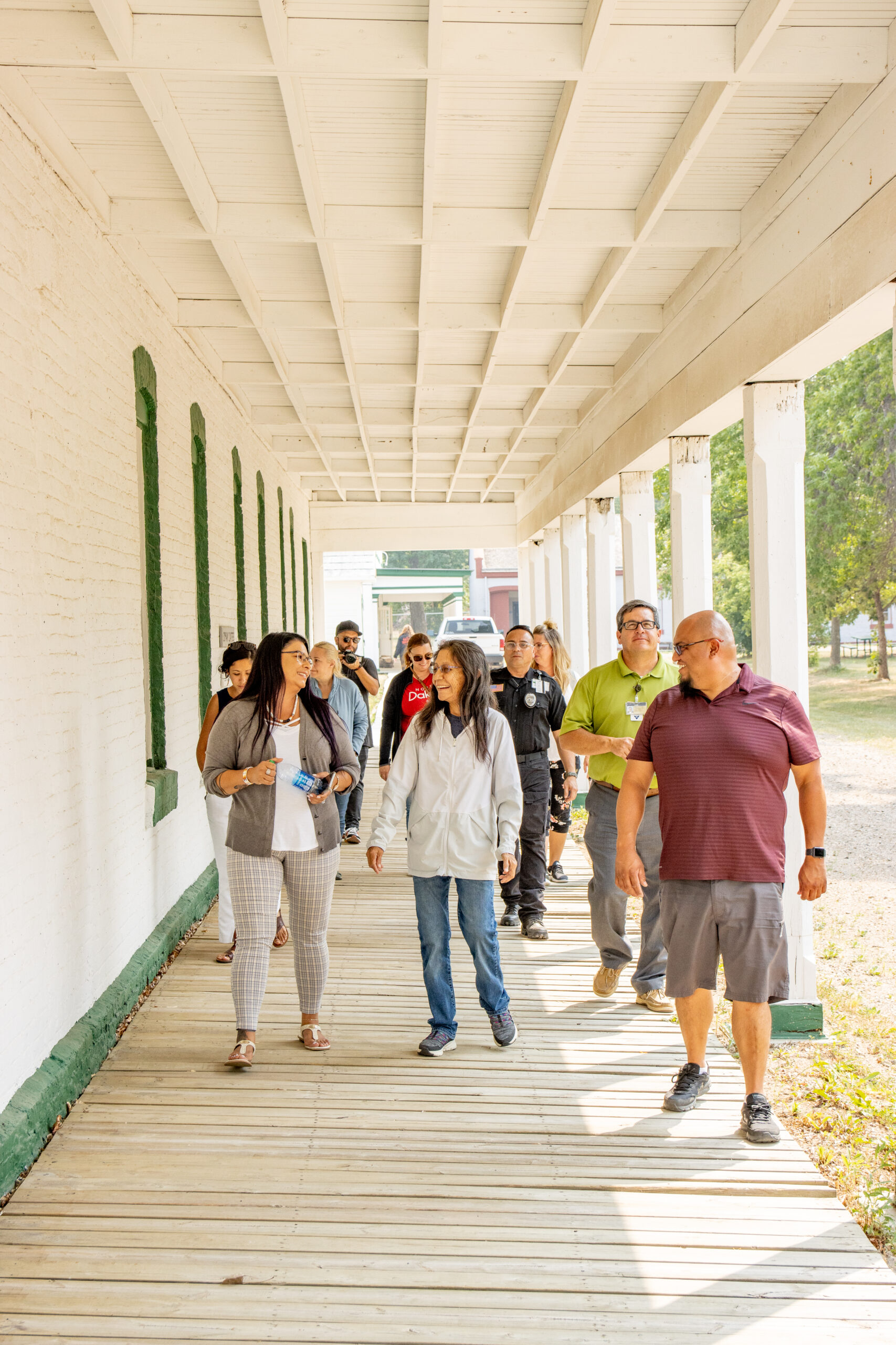 A group of people walking through a covered external corridor of a white building. Some are talking to each other and smiling.