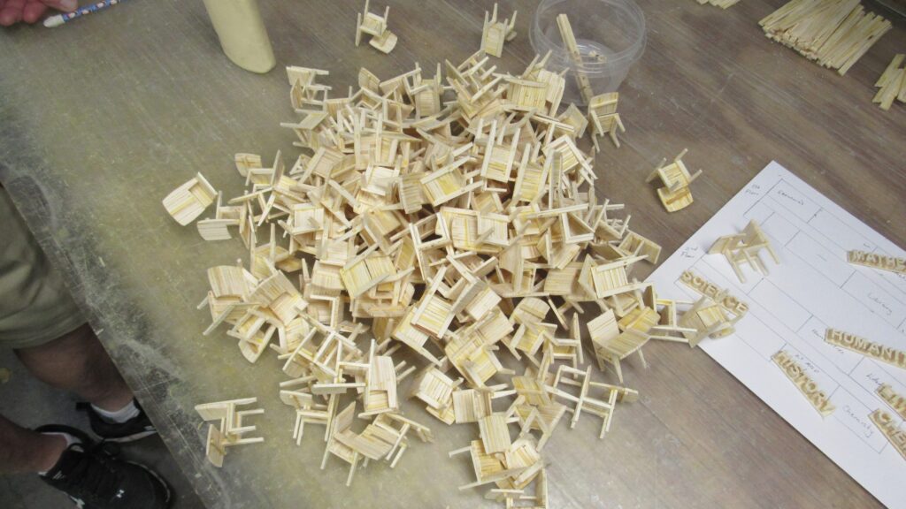 A pile of miniature chairs made of matchsticks on a table.