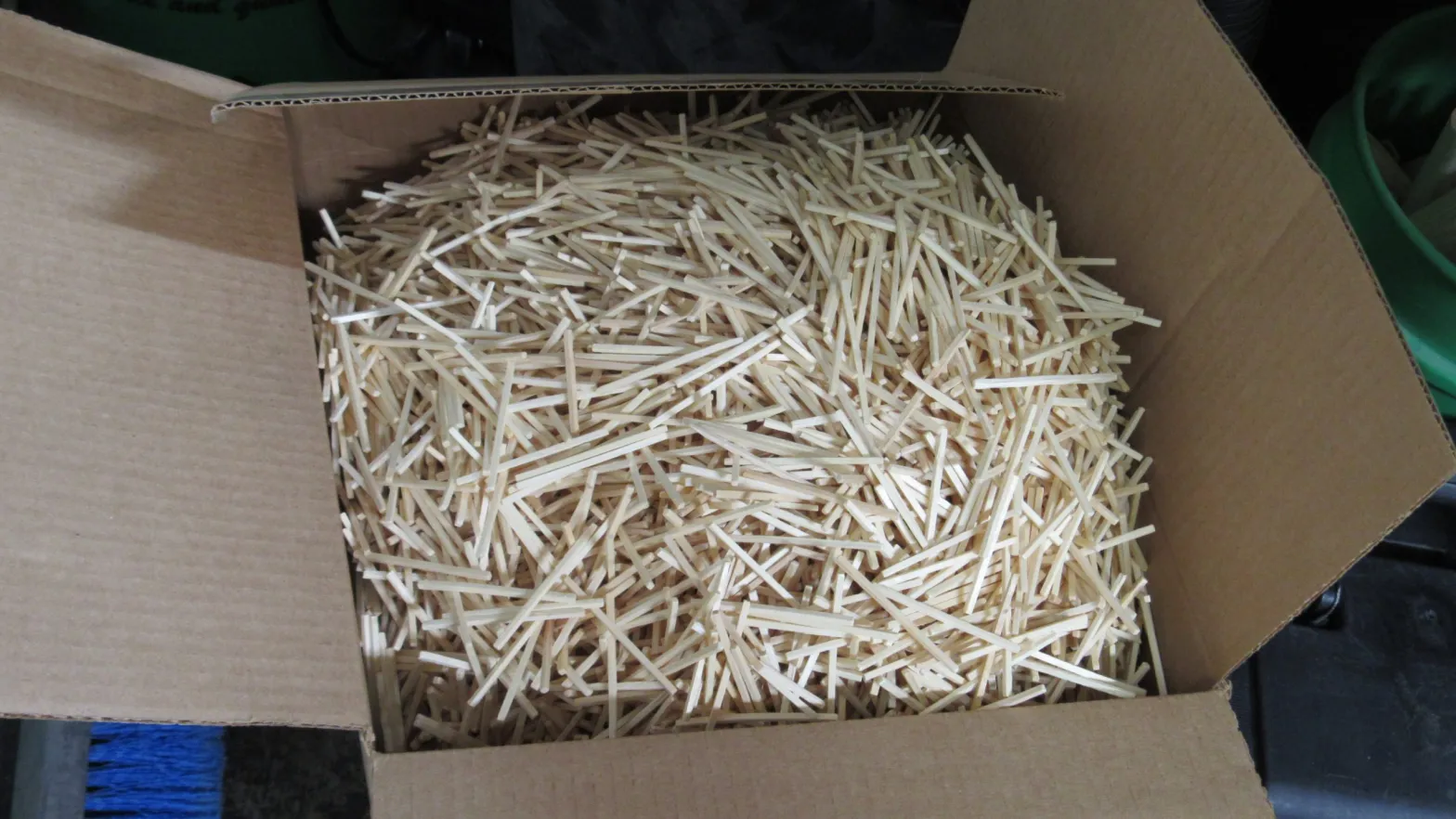 A cardboard box filled to the brim with pale wooden matchsticks sits open.