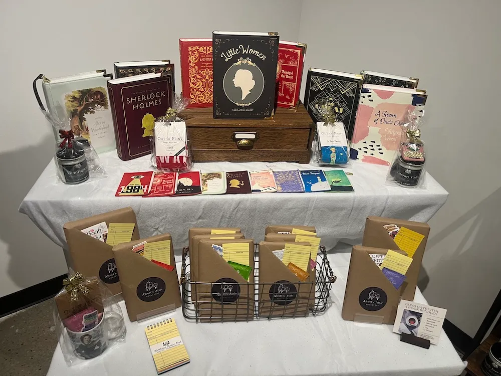 Two tiered tables with white table clothes hosts a spread of classic novels with graphic covers and other novels wrapped in brown paper packaging.