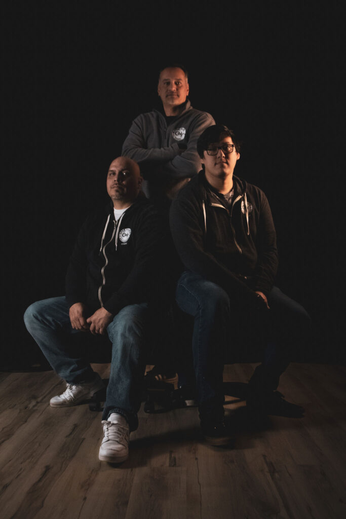 Three people sitting in a darkly-lit portrait.