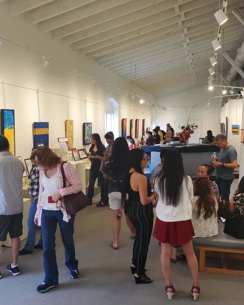 People stand around and look at artworks in a space with white walls.