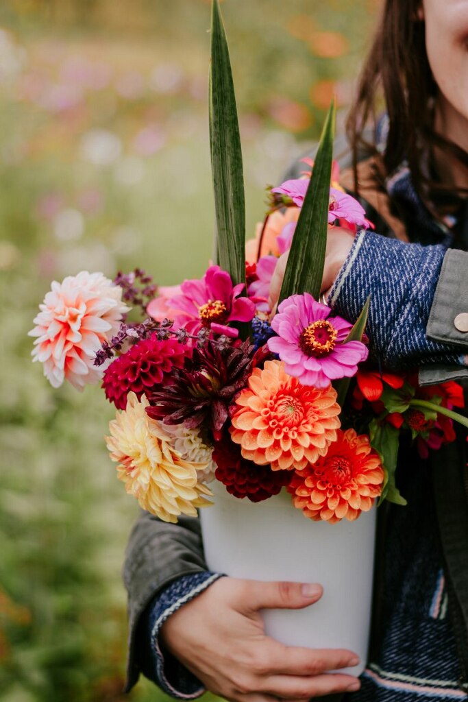 Two hands hold a white bucket filled with colorful flowers.
