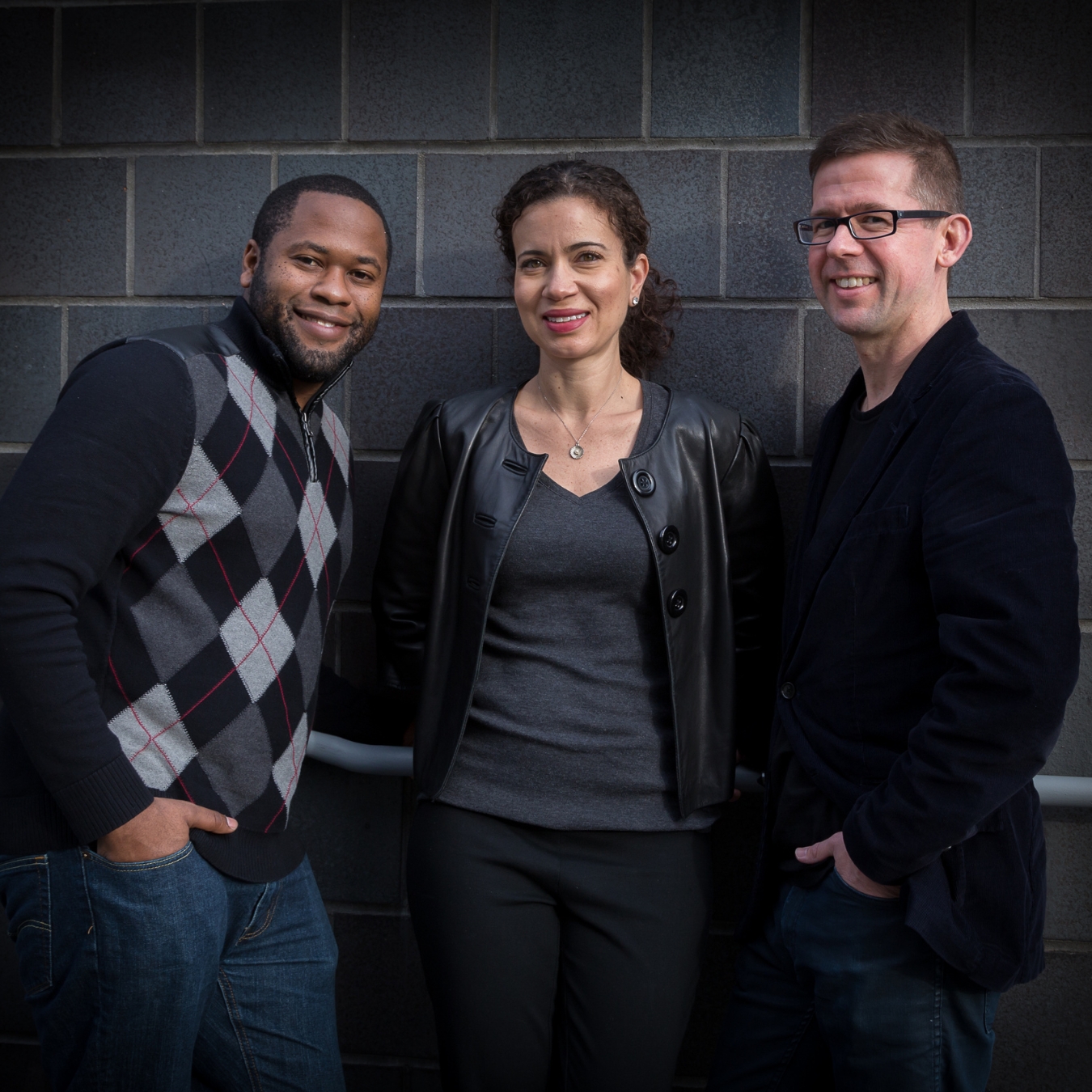 Three people smiling and posing in front of a wall.