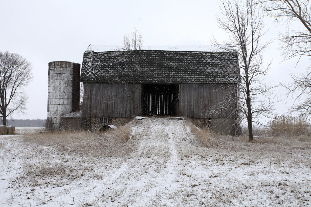 An old barn and silo in a snowy farm field.