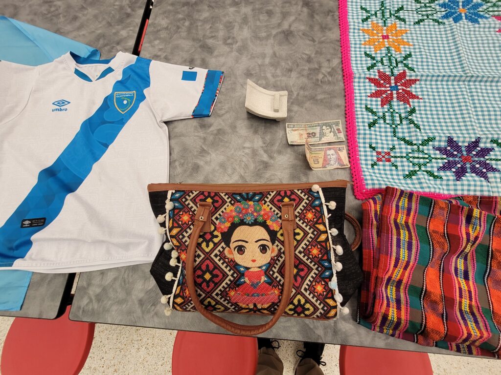 A display of objects from Guatemala, including a soccer jersey, handbag, and money.
