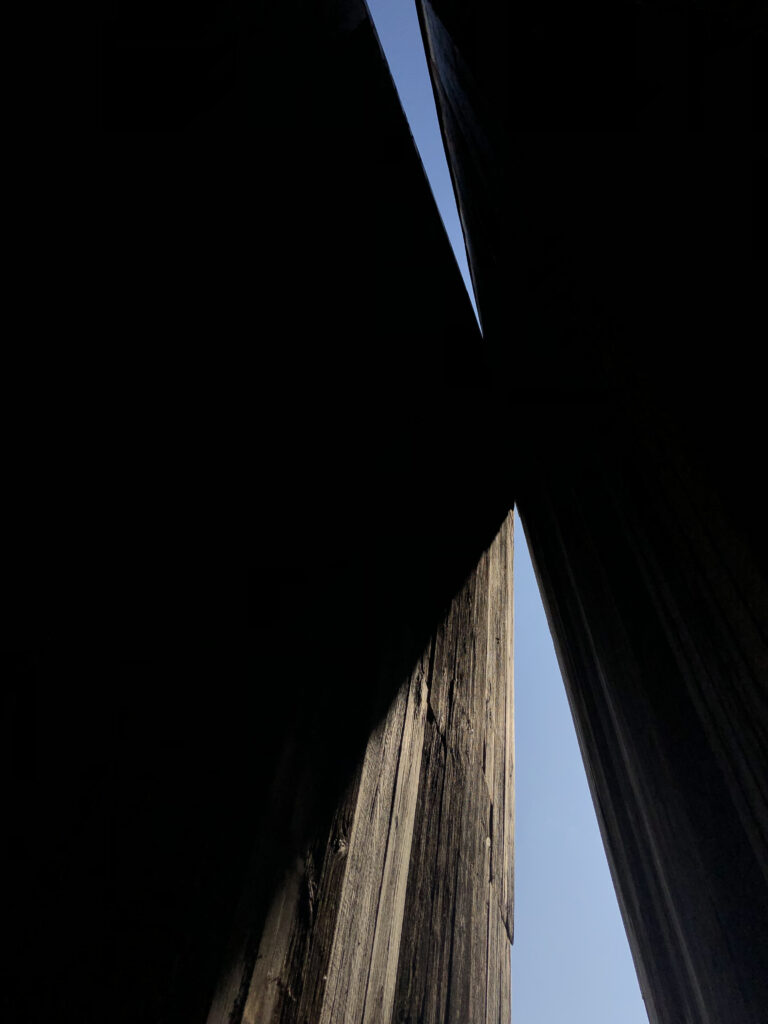 A view of blue sky through triangle shapes passages made of old barn wood.