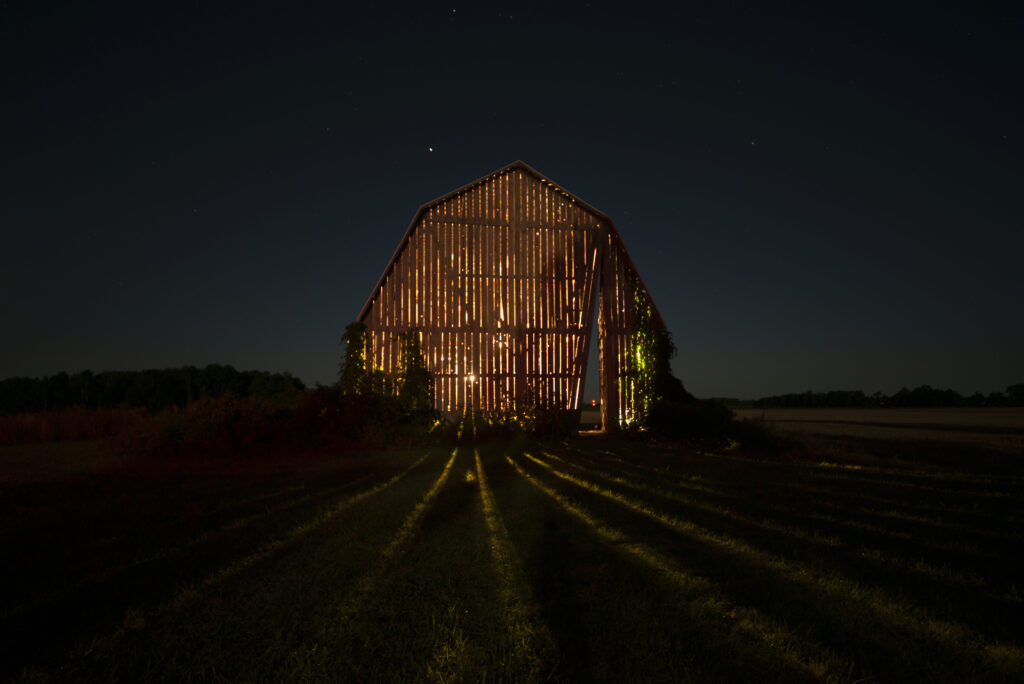 A barn with light shining through its slatted walls during nighttime.