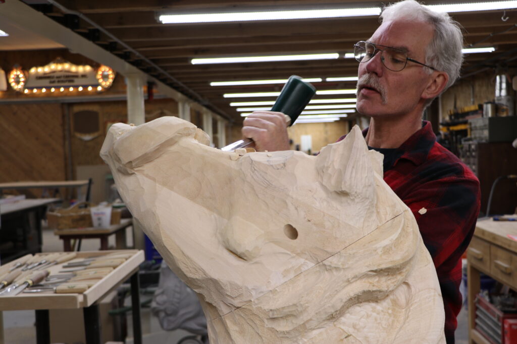 A man hand carves an elaborate wooden warthog.