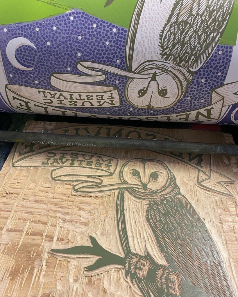 A carved woodblock depicting an owl sitting on a branch, and the poster being printed using it.