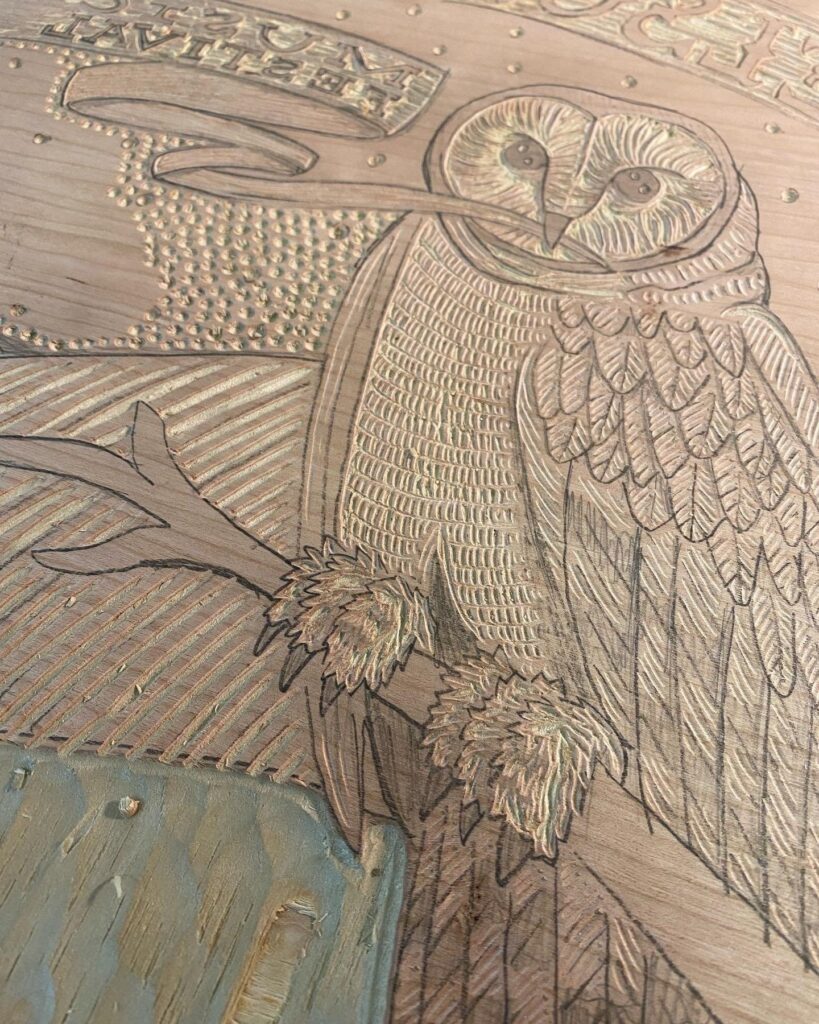A pencil drawing of an owl sitting on a branch. It is drawn on a wooden slab used for letterpress carving and printing.