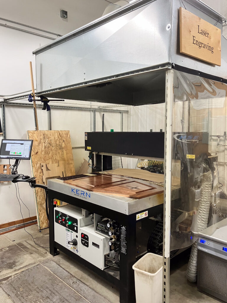 A piece of wood sits under a tall machine with a sign that read "laser engraving."