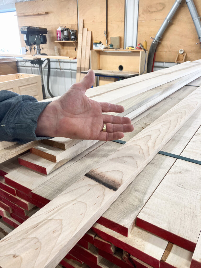 A hand gesturing to a large stack of long planks of wood.