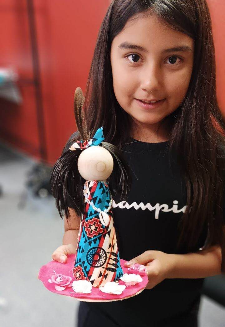 A young person of medium skin tone shows a doll wrapped in Native fabric