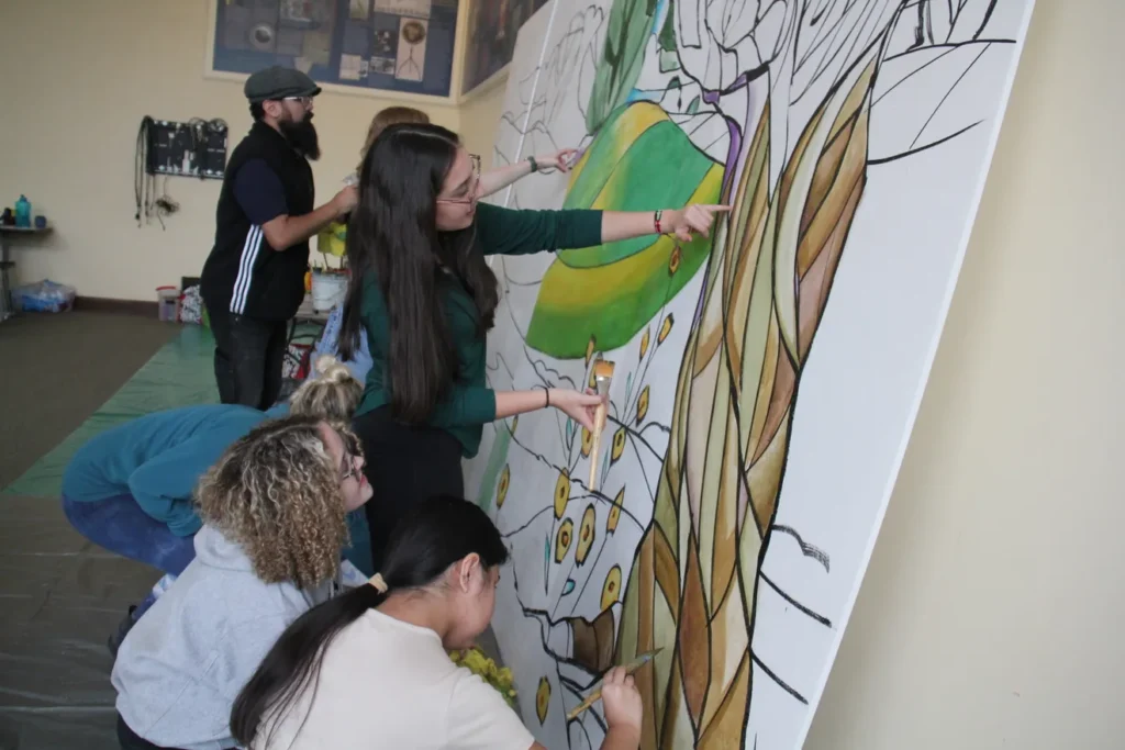 Four people add to a mural that shows a stained glass tree