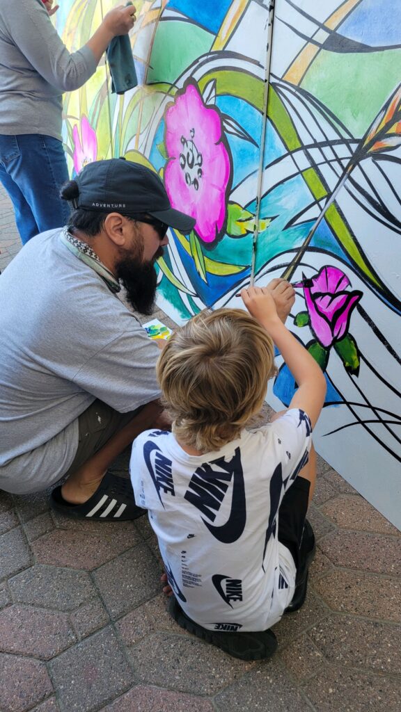 A man and a young child paint a flower on a mural together