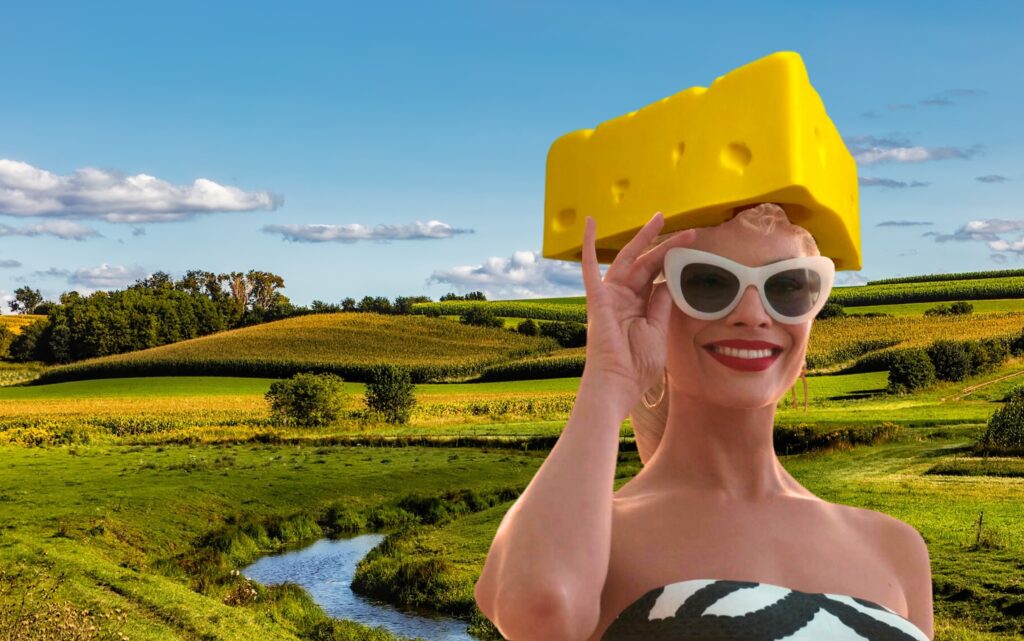 Margot Robbie as Barbie with a cheesehead hat photoshopped on, in front of a stock photo of a Wisconsin landscape.