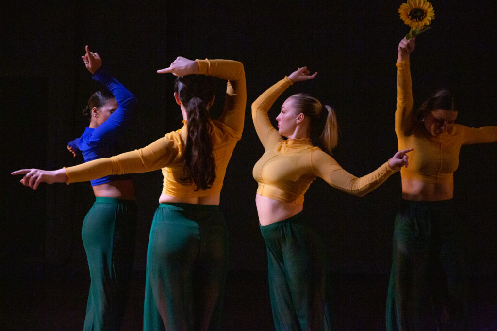Four dancers mid-performance, three dressed in yellow and one in blue