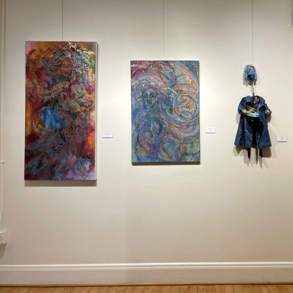 Two paintings and a fiber sculpture hung on a gallery wall.