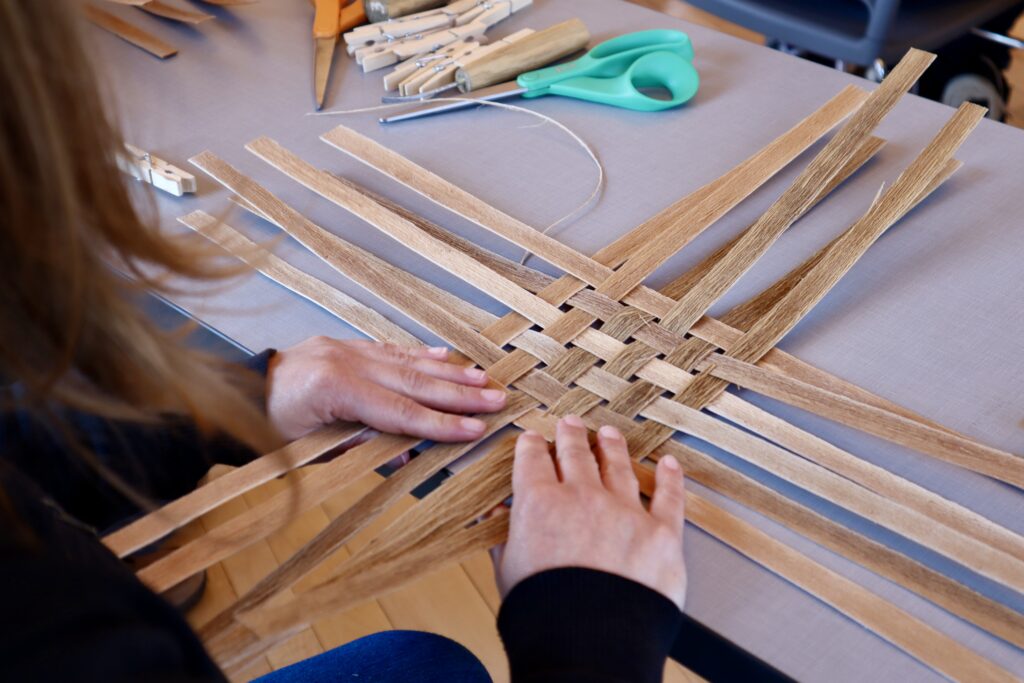 A person weaves together a basket out of black ash