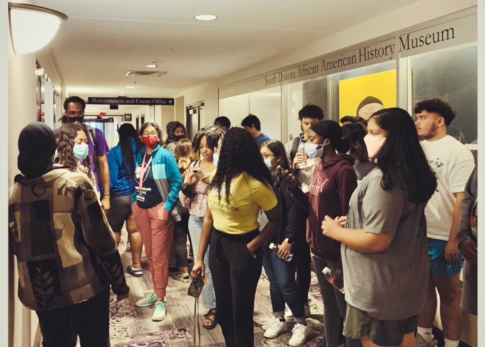 A group of about 20 young people stand in a hallway. On one side there is a glass display case with the words "South Dakota African American History Museum" above it.