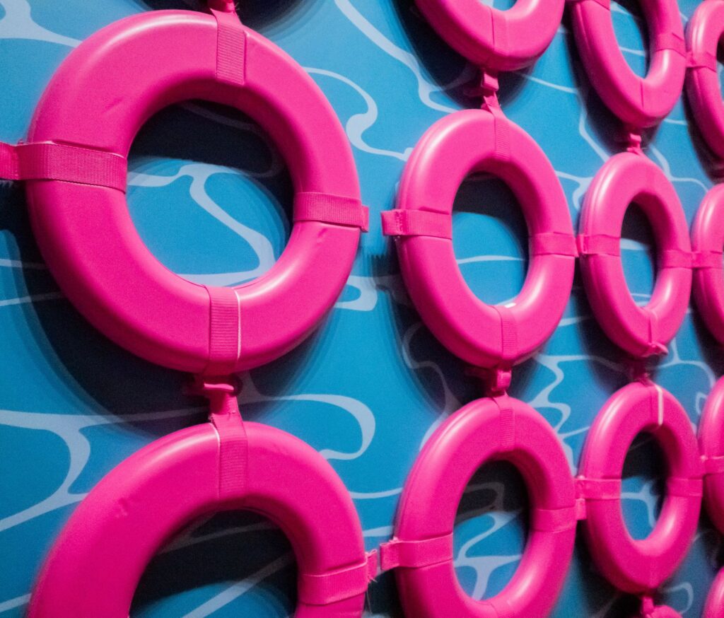 A wall painted blue to look like a pool surface with rows of pink inner tubes hung up.