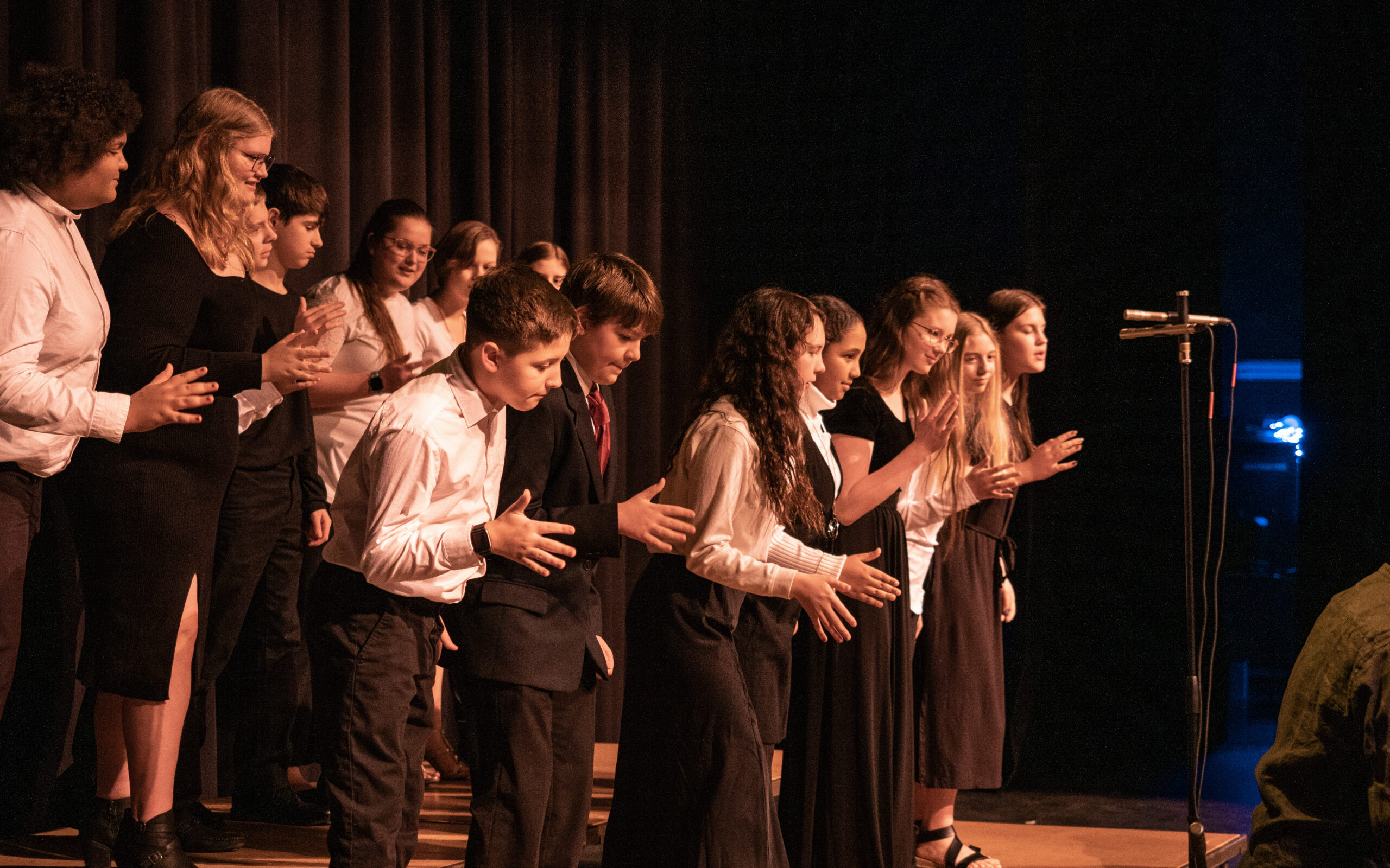 A group of middle school students dressed in a formal choir black and white clothes dance on stage