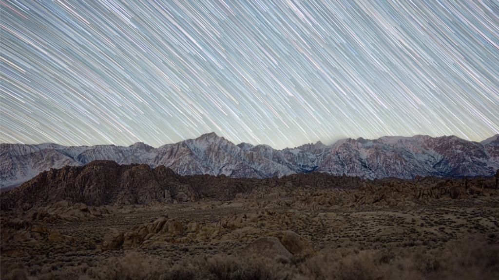 A long exposure still showing mountains with bright lines in the sky above.
