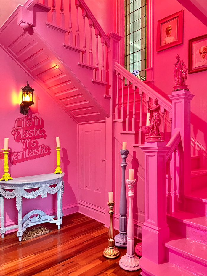 A completely pink-painted staircase with candles and a sign reading, "Life in plastic, it's fantastic."