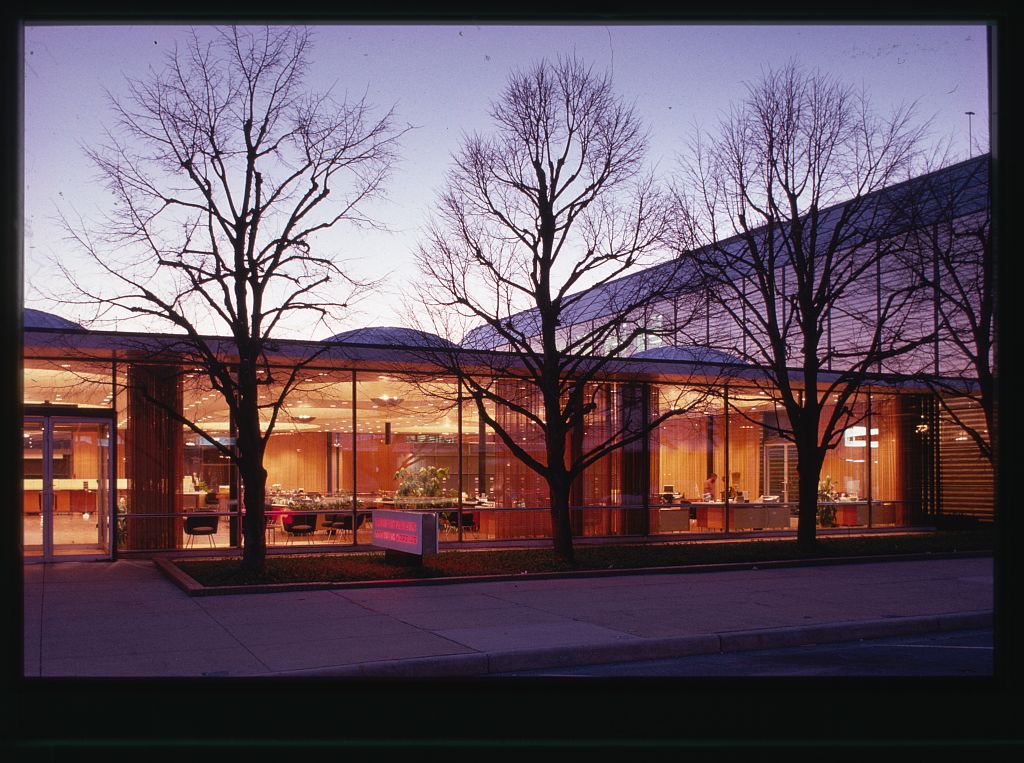 A building with large glass windows with warm lighting from the inside.