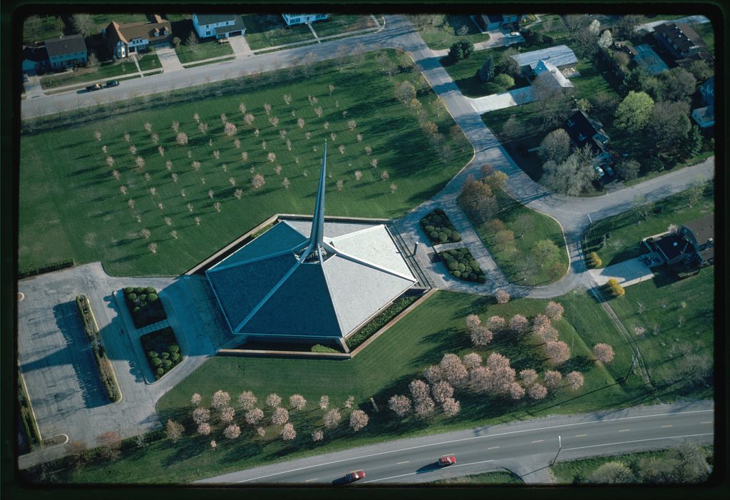 An aerial view of a distinctly shaped building with a tall needle-like architectural feature emerging from its center.