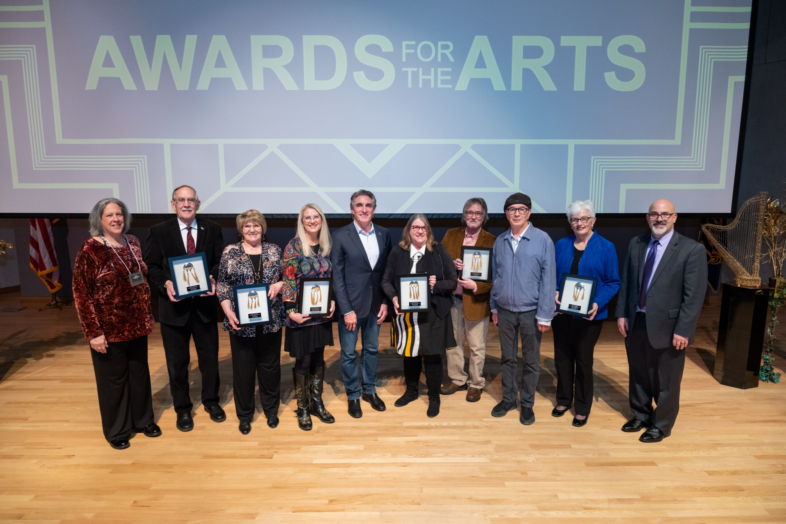 A group of people pose on a stage in front of a sign that says Awards for the Arts
