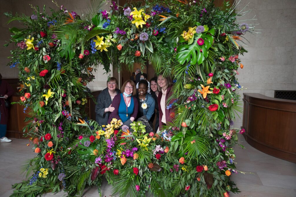 A giant frame made out of flowers with a group posing in the middle